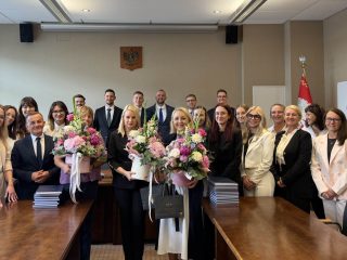 Zdjęcie grupowe po obronach prac dyplomowych w sali konferencyjnej, z bukietami kwiatów.