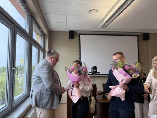 Uczestnicy obron wręczają komisji bukiety kwiatów zapakowane w różowy papier.