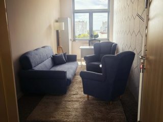 Gabinet poradni z granatową sofą, dwoma fotelami i małym stolikiem.