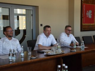 Trzej mężczyźni w białych koszulach siedzący przy stole konferencyjnym podczas spotkania z KGHM INOVA.