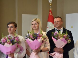 Trzy osoby pozują z bukietami kwiatów w sali UJW podczas spotkania z okazji obron zarządzania.