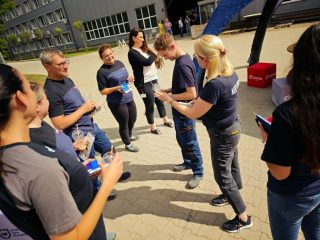 Grupa pracowników i gości rozmawia na placu przed halą.