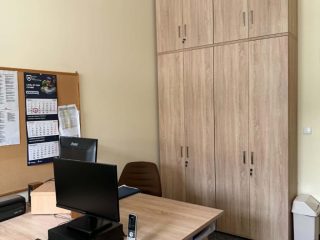 Stanowisko biurowe z laptopem i drukarką obok wysokiej szafy.