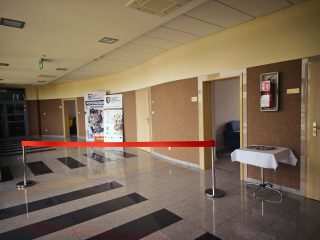 Korytarz przed gabinetami poradni z czerwoną wstęgą i stolikiem.