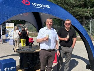 Dwaj mężczyźni z napojami stoją przed namiotem z logo INOVA.