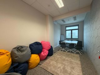 Sala z kolorowymi pufami oraz stołem i krzesłami przy oknie.